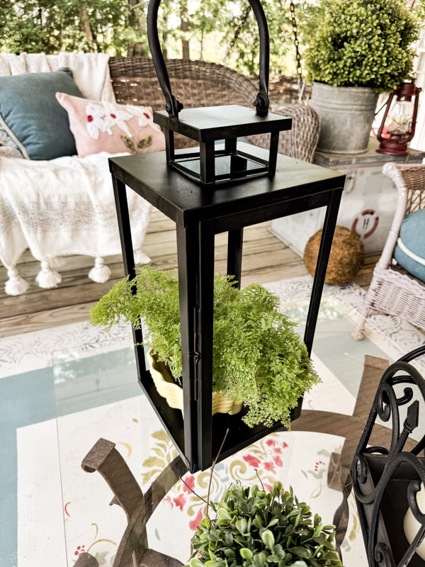 Repurposed outdoor lantern painted black with vintage yellow planter filled with green fern.