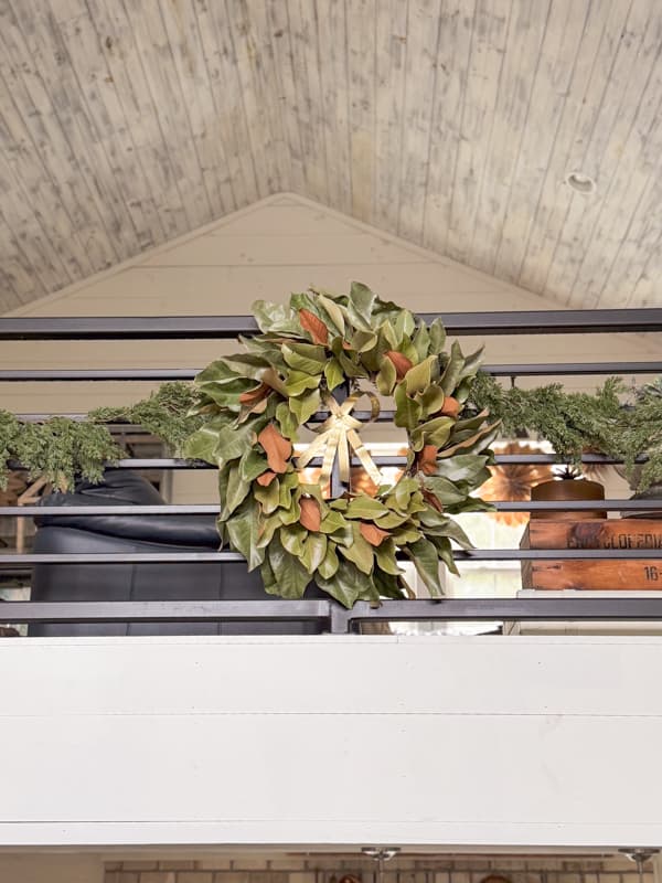 DIY fresh magnolia leaf wreath with gold bow on loft banister railing for Christmas after several weeks.