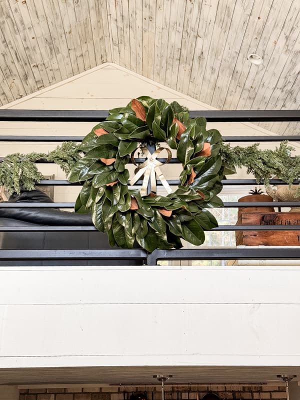 DIY fresh magnolia leaf wreath with gold bow on loft banister railing for Christmas.  