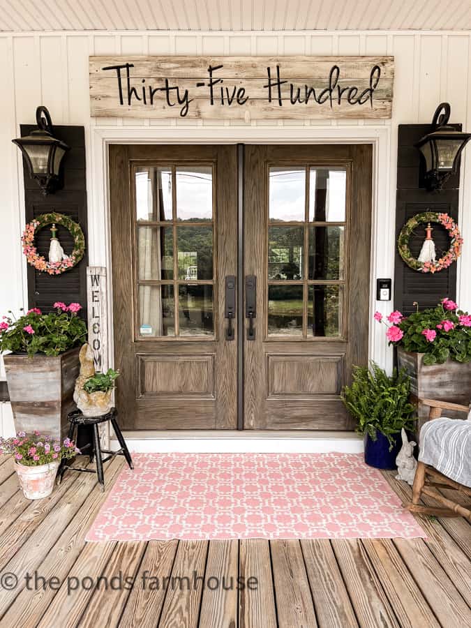 https://www.thepondsfarmhouse.com/wp-content/uploads/2023/06/Country-Porch-French-front-doors-with-pink-rug-and-address-sign-2.jpg