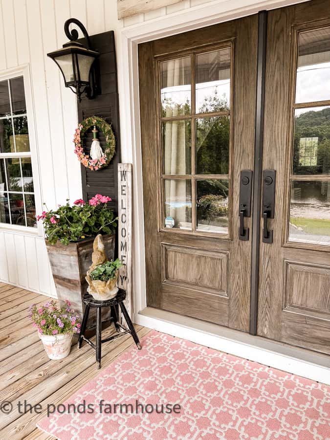 https://www.thepondsfarmhouse.com/wp-content/uploads/2023/06/Country-Porch-French-front-doors-with-pink-rug-planters.jpg