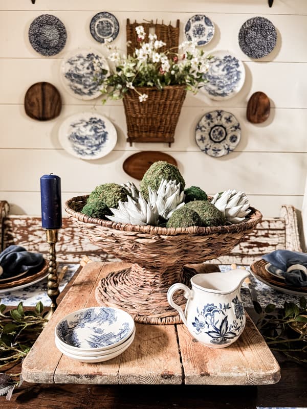 basket centerpiece on dining room table with moss and artichoke decor.