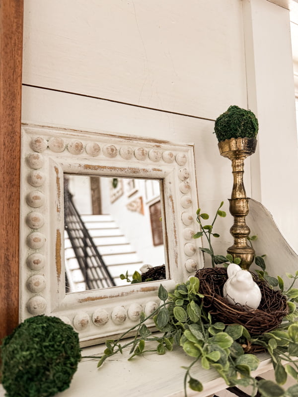 The beaded wood frame is tucked behind a shelf vignette with vintage candlestick holder and bird nest.  
