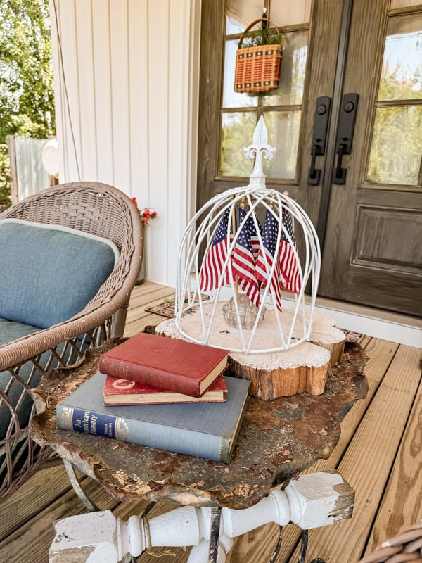 American flags under garden metal cloche with vintage books on side table on porch