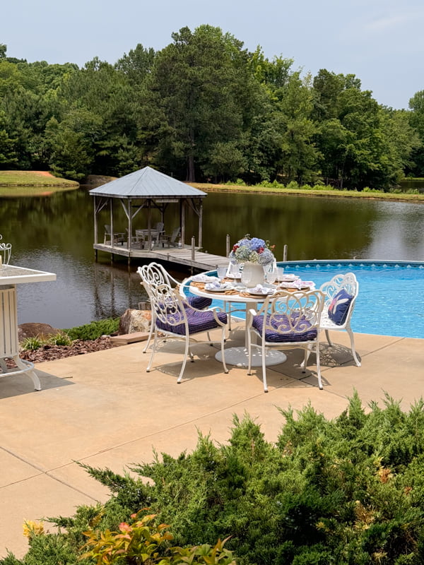 poolside dining table with thrifted white cast aluminum table and chair and gazabo pier on the pond. 