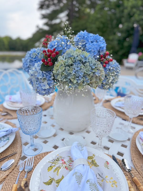 Blue hydrangea centerpiece in ironstone vase with baby's breath and red berries.  
