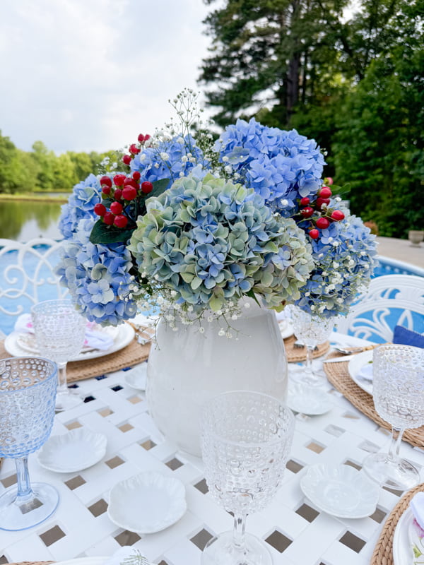 Blue hydrangea centerpiece in ironstone vase with baby's breath and red berries.  