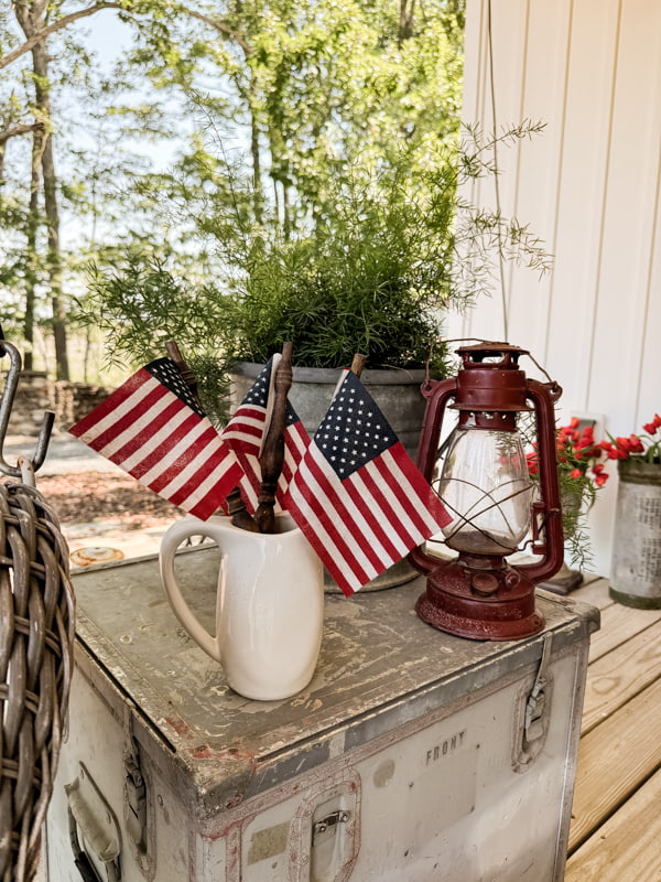 American flags on vintage spindles in a ironstone pitcher on metal side table for front porch decorations.