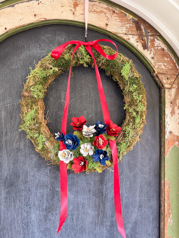 Patriotic Summer time Wreath idea with a moss frame with red, white and blue painted pinecone flowers and red ribbon.