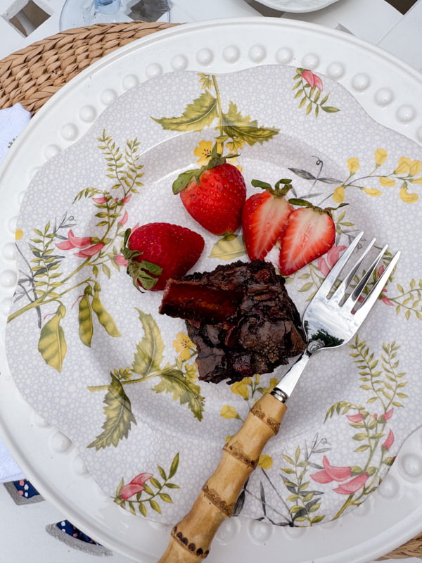Smoked Salted Caramel Dark Chocolate Brownies with candied bacon and strawberries on botanical plate.