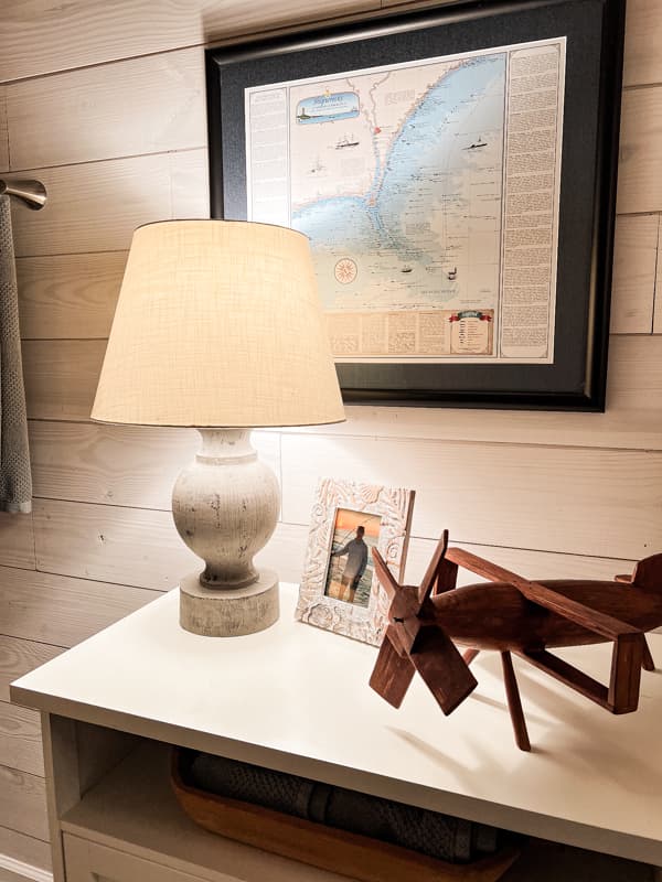 Coastal lamp on chest in bathroom with coastal decor.