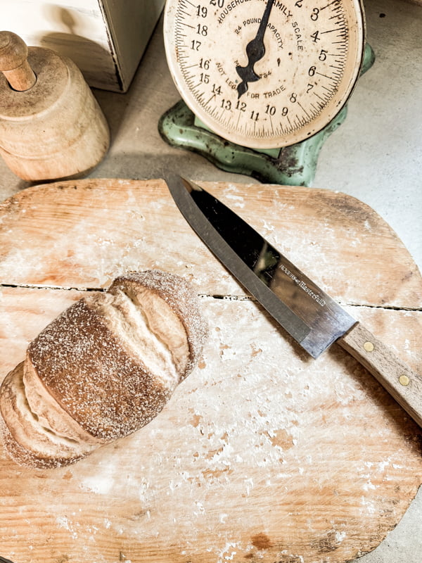 Old Breadboard with crusty dough and loaf of bread and knife.  Vintage scale and butter mold.  