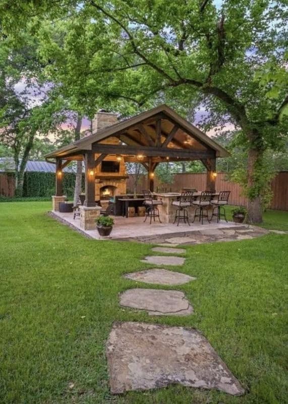 Rustic outdoor kitchen structure with stone pavers in grass.