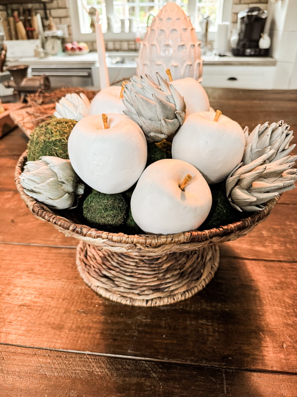 Bowl of apples with moss balls and artichokes in a woven wicker basket