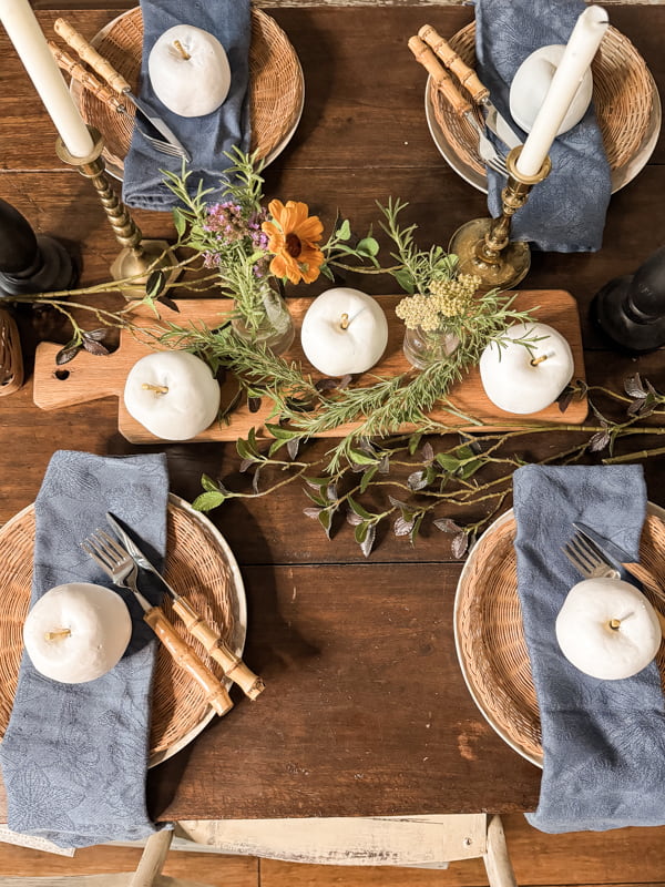 White Apple Centerpiece on Rustic Tablescape with wicker plate chargers and bamboo cutlery.