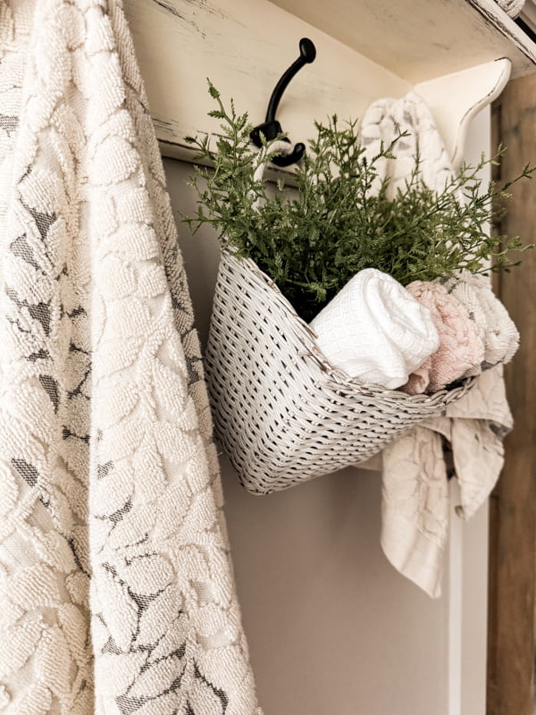 Bathroom wall shelf with basket of hand towels and greenery. 