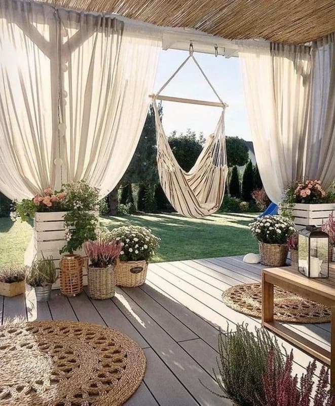 Cozy front porch with gauzy white curtains, swing and rattan rugs.  Pallet Planters and baskets filled with plants.