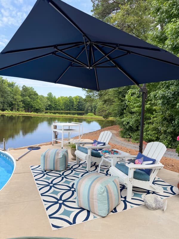 Poolside outdoor living area with umbrella, adirondack chairs, rug and puff ottomans.