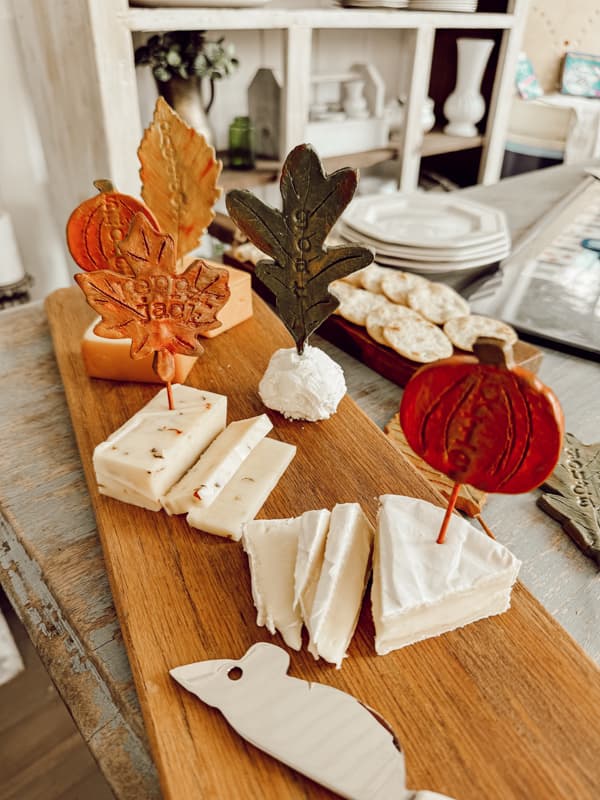 Handmade cheese markers in the shape of fall leaves and pumpkins on cheese board with crackers