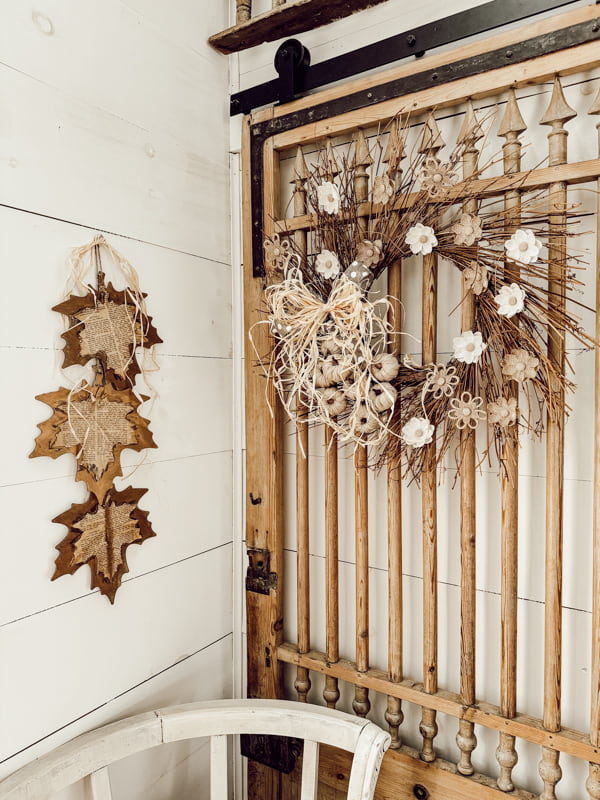 DIY Dollar Tree Wreath with Burlap Flowers and Pumpkins on the barn door next to wood and old book page leaves. 