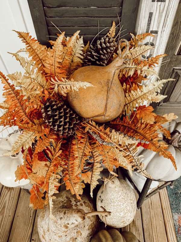 planter filled with fall ferns, pinecones and dried gourds. 