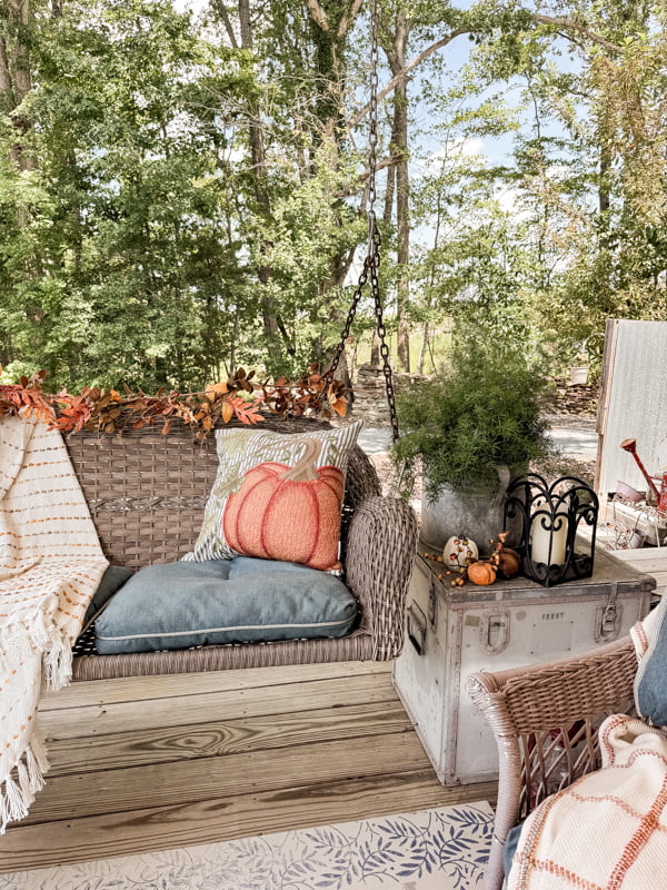 Porch swing with pumpkin pillow and throw blanet with blue cushions.  Swing draped with a fall leaf garland.  