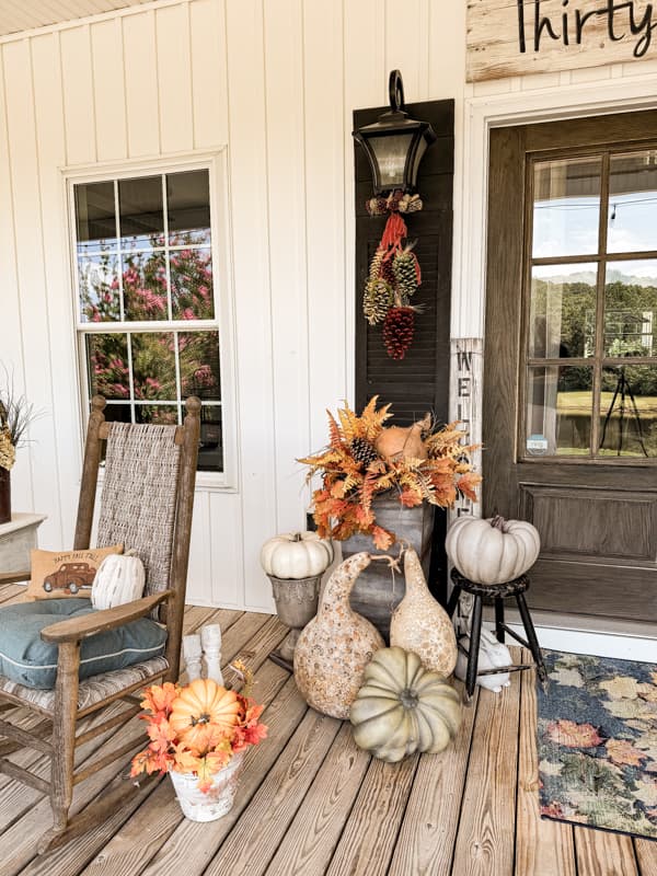 Planter on front porch surrounded by dried gourds, and faux pumpkins.  