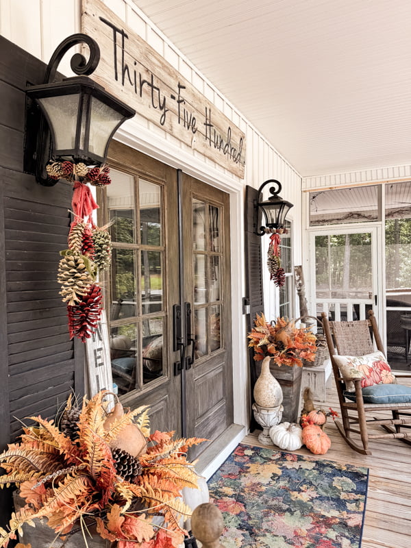 Pinecone Swags for fall front porch decor.  Planters with fall ferns and gourds with a leaf porch rug.  