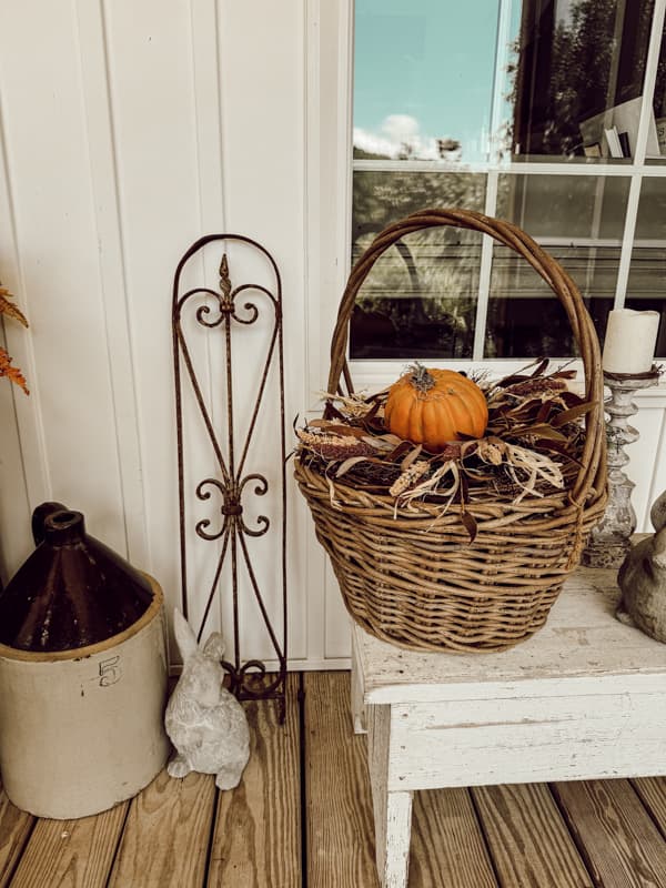 Vintage basket for fall porch decorating with orange pumpkin and vintage stone jug.