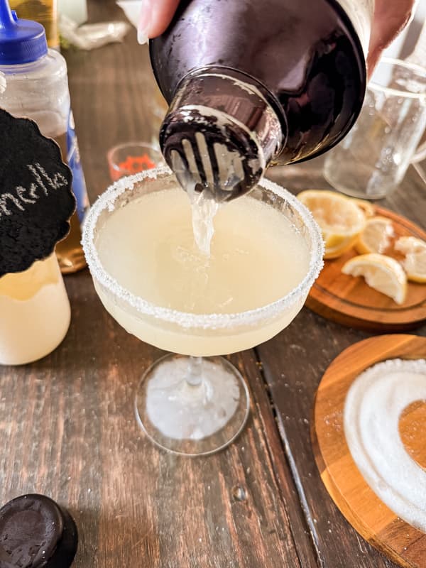 Pour lemon drop martini recipe with a strainer to reserve ice into a sugar rimmed cocktail glass.