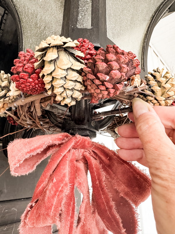 Attach grapevine pinecone wreath to light fixture with small twigs to secure for pinecone swag 