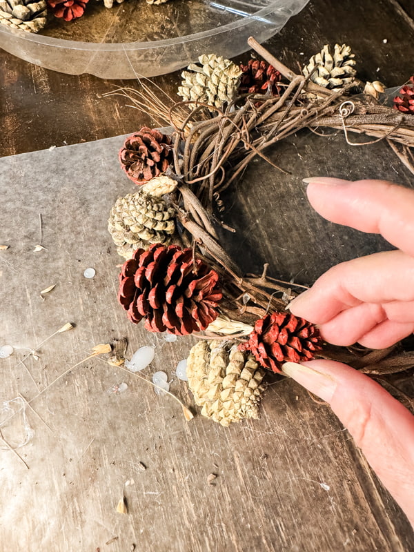 Use hot glue to attach small pinecones to the foraged grapevine wreath.