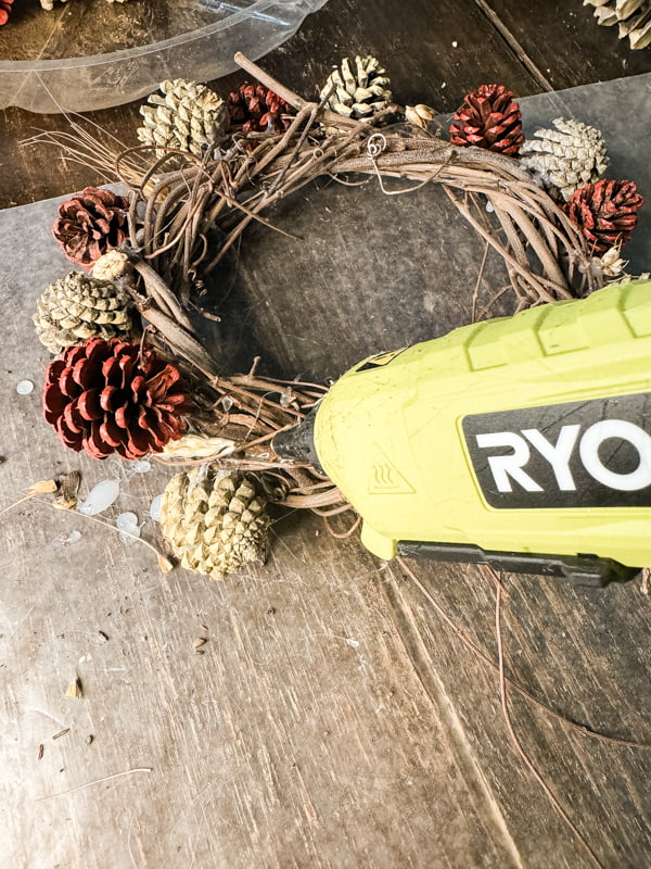 Use hot glue to attach small pinecones to the foraged grapevine wreath.