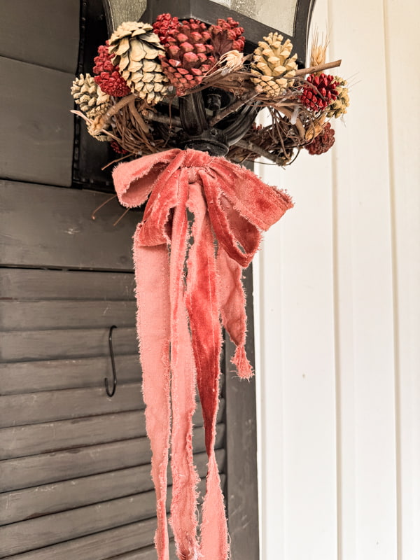 frayed velvet ribbon tied to wall sconce light fixture with grapevine pinecone wreath around the bottom.