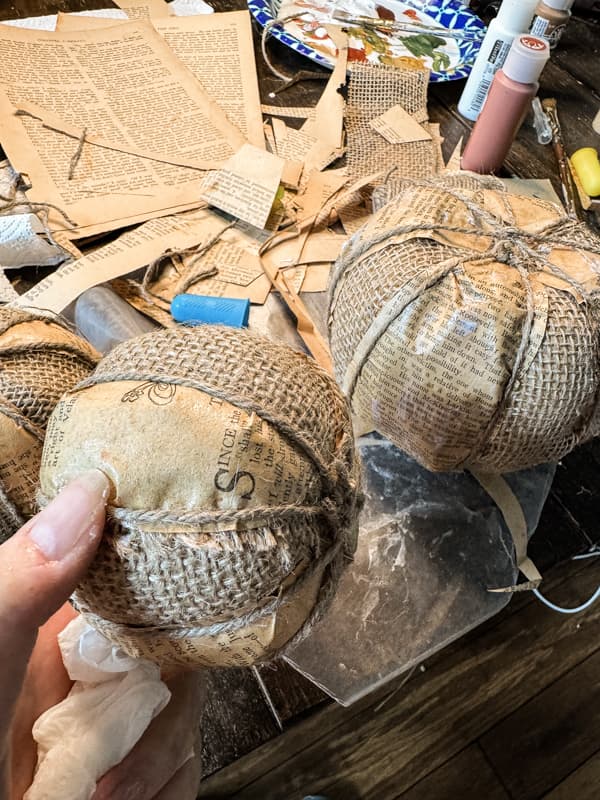 Wrap burlap pumpkins with jute twine to hold the old book pages in place for a primitive fall craft.