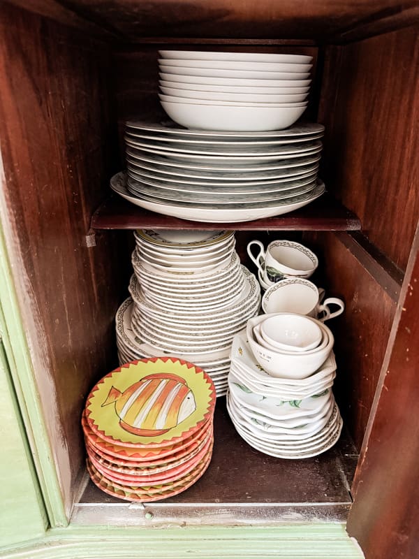 Stacked vintage dishes in deep cabinet.