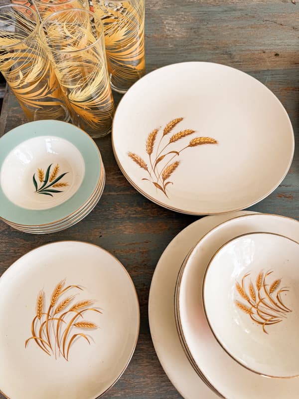 Vintage dinnerware plates, bowls, and glasses on farmhouse table.