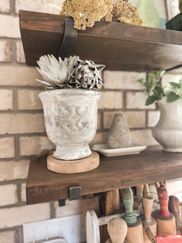 Upcycled Decor vase on open kitchen shelf with faux dried artichoke and a concrete pear.