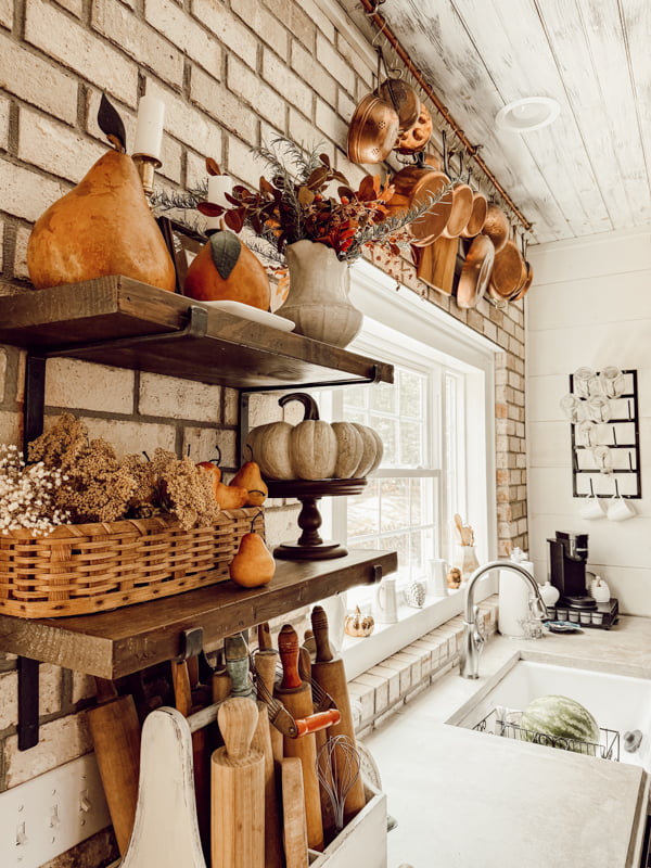 Open shelves filled with fall home decorations and copper pot hanging rack on brick wall