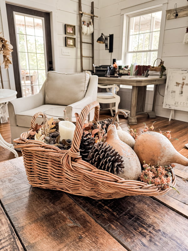 Large basket centerpiece filled with gourds, pinecones and fall stems with a hurricane lantern from thrift store