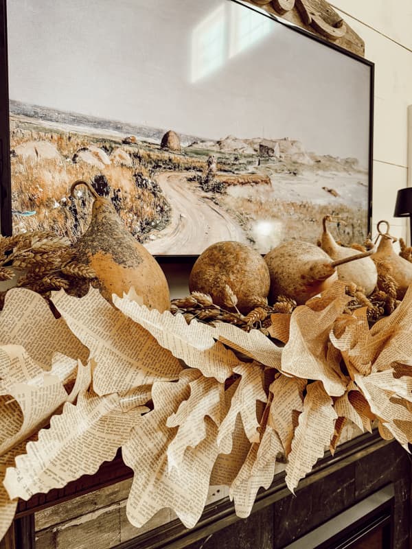 Dried gourds and old book page fall leaf garland on mantel. 