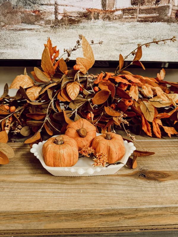 white milk glass with small pumpkins and fall mantel garland