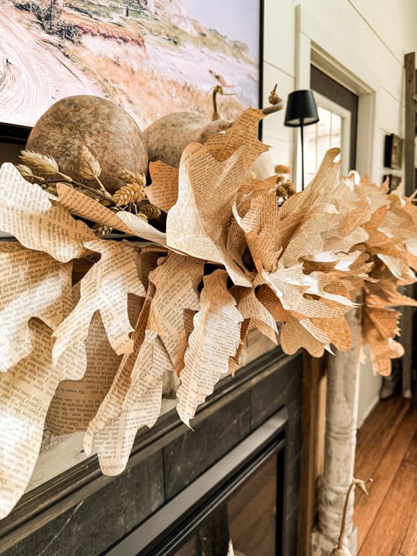 Rustic DIY Fall Leaf Garland made with upcycled old book pages on fall mantel with dried gourds.  