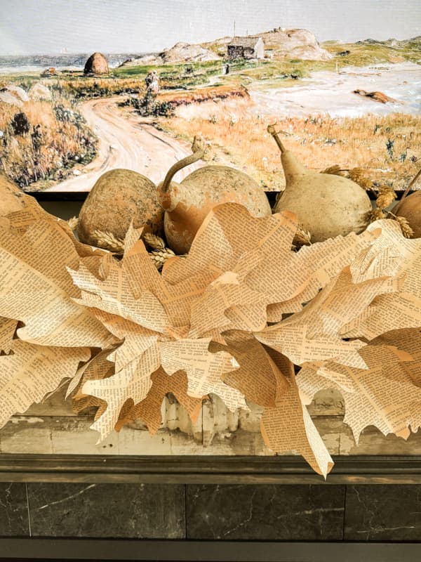 Rustic DIY Fall Leaf Garland made with upcycled old book pages on fall mantel with dried gourds. 