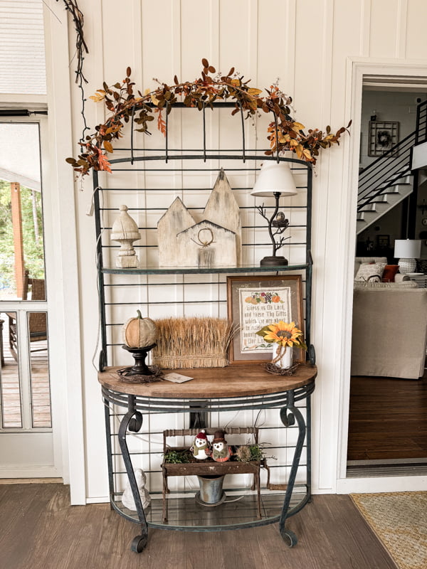 Bakers rack decorated on screened in porch. Wooden village and fall decor.