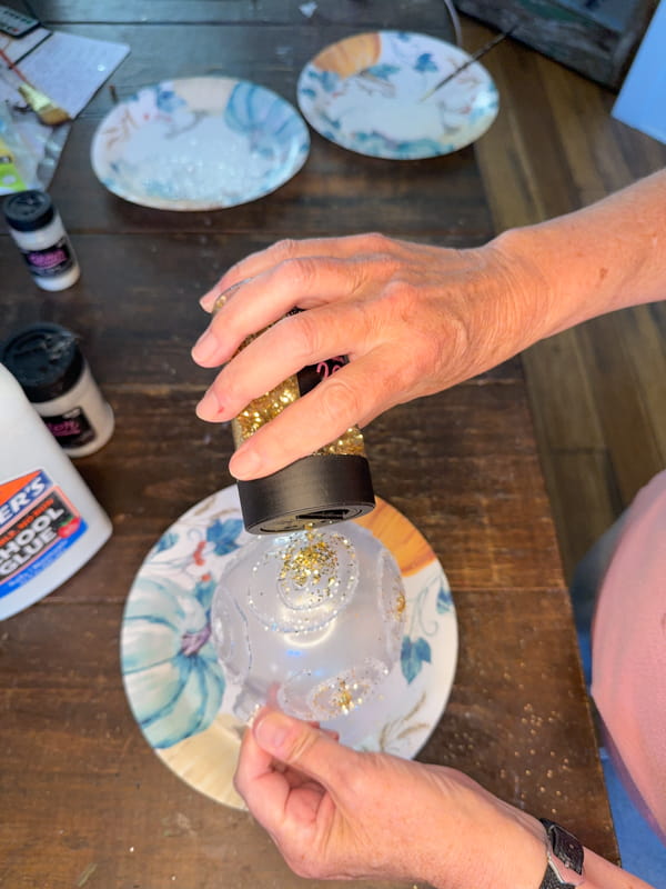 Sprinkle gold glitter on glue in small sections of the DIY Christmas Ornaments.