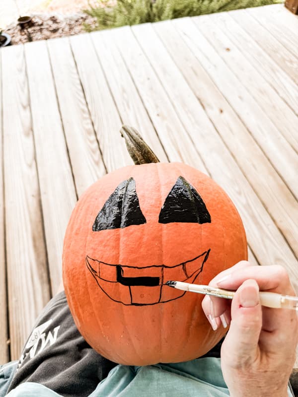 Paint Jack O' Llantern face on pumpkin with black craft paint.