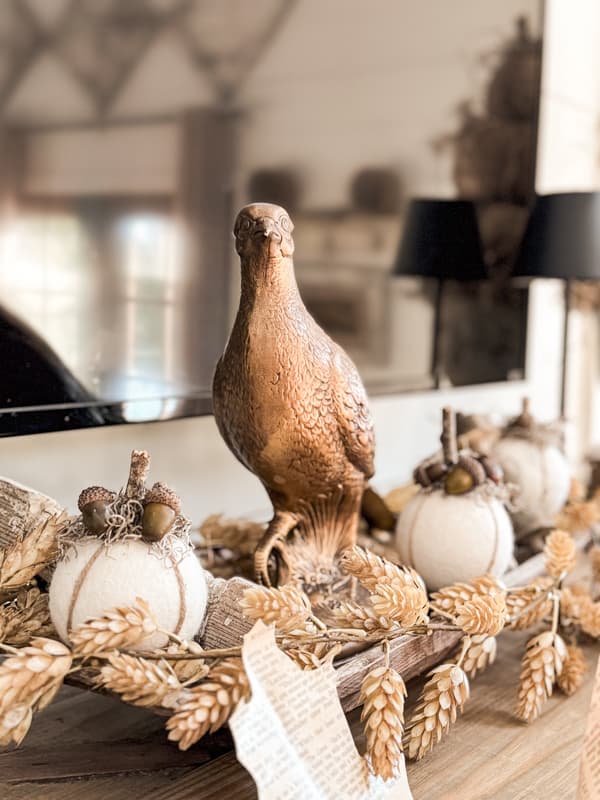 Trio of fall pumpkins mixed with architectural elements and a gold pheasant on the mantel.  