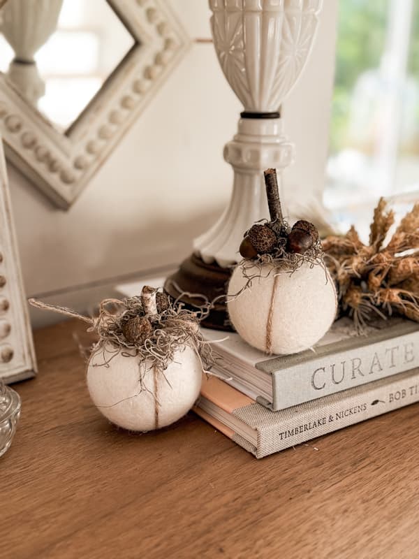 two wool pumpkins on entry table  with books and milk glass lamp.