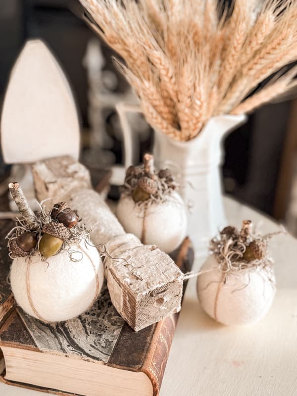 Three pumpkins grouped together on side table with ironstone pitcher full of dried wheat.  